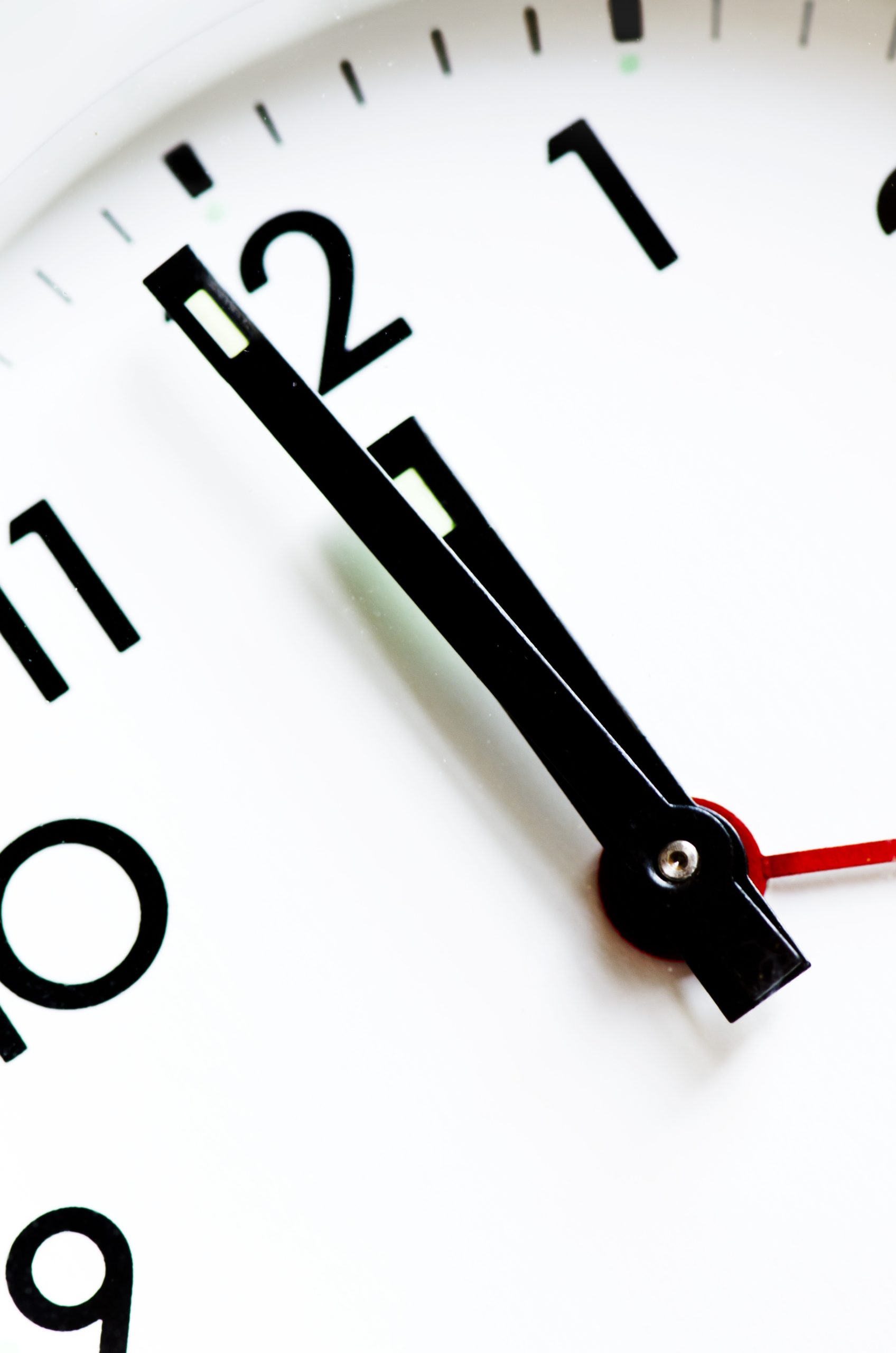 Nahaufnahme des Ziffernblattes eines Weckers. Die Zeiger stehen auf kurz vor zwölf Uhr.